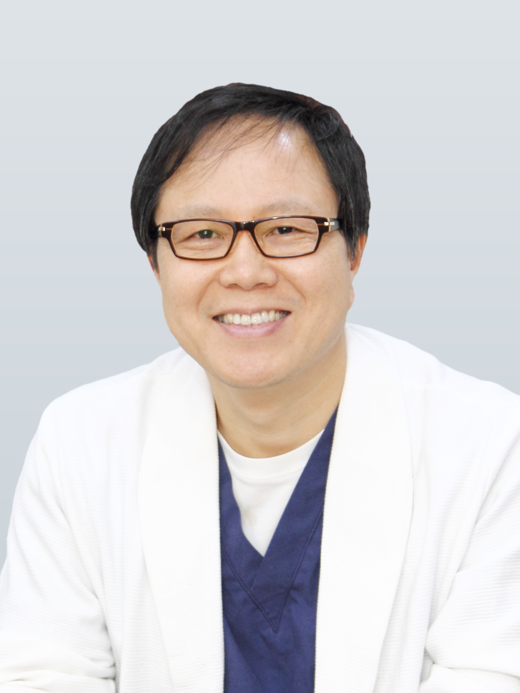 흰 가운과 남색 수술복 차림으로 안경을 쓰고 웃고 있는 한동균 원장